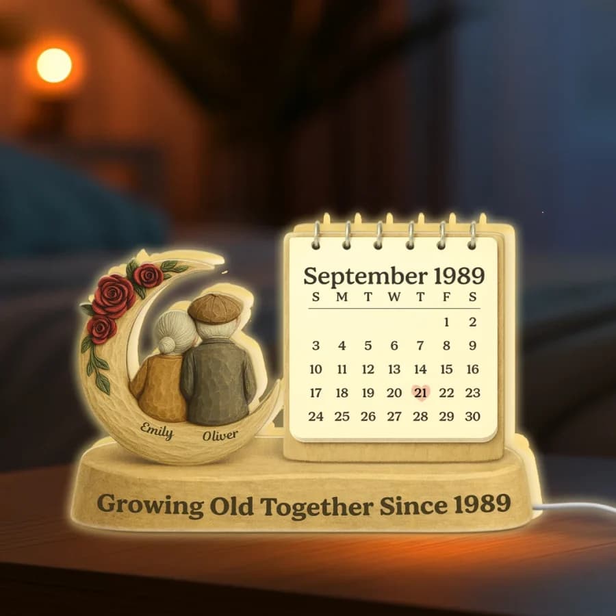 A warm-lit wooden lamp showing a couple on a crescent moon beside a calendar page for September 1989 with the 21st marked by a heart